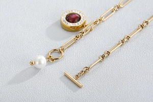 Macro shot of gold necklace with red gemstone ring, white pearl, and toggle clasp