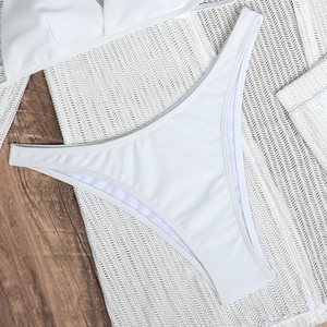 Flat lay detail of white high-cut bikini bottoms on mesh beach cover-up and wood