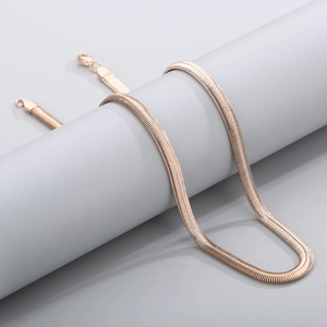 Sleek gold-plated flat snake chain necklace displayed on a minimalist gray pillar stand