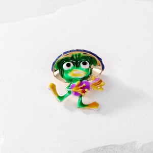 Detailed close-up of a cute green frog enamel pin with a blue hat on a white texture