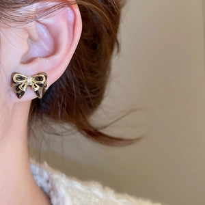 Close-up of a model wearing minimalist black and gold bow earrings with crystal accents