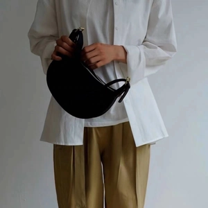 Detail view of a black leather crescent saddle bag held by a model in a minimalist style