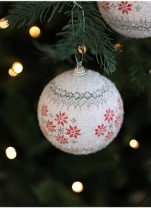 Close-up of a white foam Christmas ball with red snowflakes and glitter on a tree