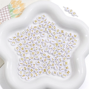 Macro shot of 4x7mm white acrylic alphabet beads with gold letters in a star ceramic dish