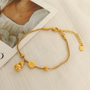Gold stainless steel bracelet with Fu character and gourd pendant on textured fabric