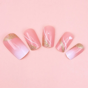 Detail of pink and white gradient press-on nails with gold glitter and heart accents