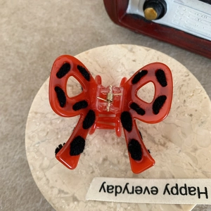 Close-up of a red bow hair claw clip with black plush polka dots on a marble tray