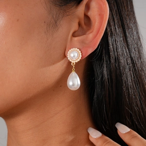 Macro view of gold pearl earrings featuring large round stud and teardrop pearl pendant