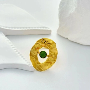 Detailed close-up of a gold geometric ring with a green gemstone on white art props
