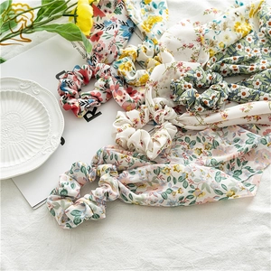 Close-up of assorted floral chiffon hair scrunchies with long ribbons on white fabric