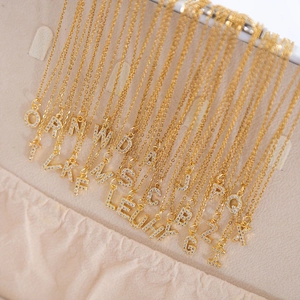 Gold square initial necklace with cubic zirconia pave letters on beige textured fabric
