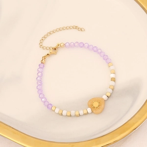 Detail of beaded heart bracelet with purple faceted stones and gold sun charm pendant
