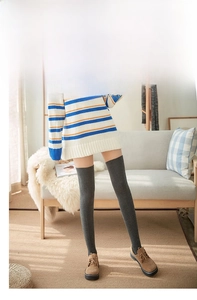 Detail of dark grey over-the-knee knit socks styled with brown loafers in a cozy setting
