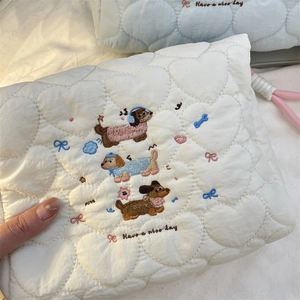 Close-up of heart quilted cream makeup bag featuring cartoon dog embroidery and lettering