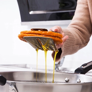 Stainless steel kitchen tongs lifting fried food showing oil drainage function in action