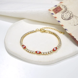 Close-up of golden zircon bracelet with red enamel evil eye charms on vintage postcard