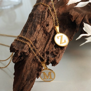 Goldene Buchstabenkette mit weißem Muschel-Anhänger auf Holz präsentiert