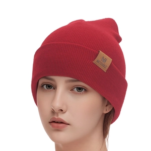 Detail of red ribbed knit beanie showing the M METERULE leather patch texture