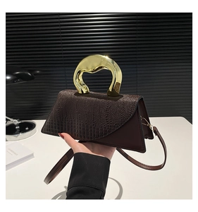 Detail of dark brown handbag featuring crocodile texture and unique gold metal handle
