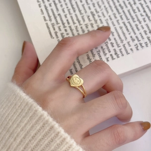 Macro view of a gold heart smiley face ring worn over a cozy white knitted sleeve