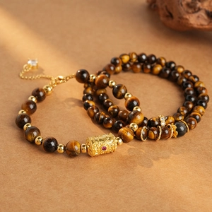 Macro detail of tiger eye beads with golden hollow cylinder charm and red gem inlay