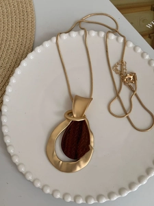 Detail of geometric teardrop pendant with matte gold frame and wood grain inlay on snake chain
