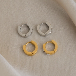 Détail de boucles d'oreilles créoles or et argent avec zircons sur tissu beige