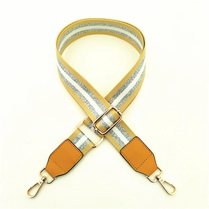 Detail view of adjustable wide fabric bag strap with yellow stripes and gold metal hardware