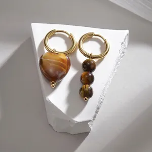 Détail macro de boucles d'oreilles asymétriques en or avec pierres œil de tigre polies
