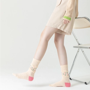 Beige crew socks with floral embroidery and pink heel patches in a minimalist studio setting
