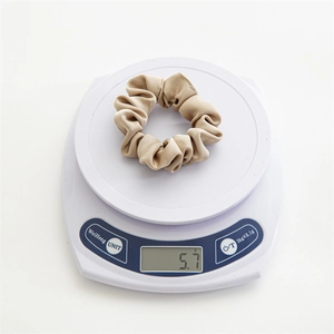 Détail du poids montrant un chouchou en satin de 5,7g sur une balance numérique beige