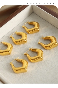 Detail view of bold gold geometric U-shaped earrings on a wooden jewelry display tray