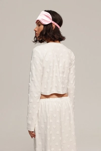 Détail d'un ensemble homewear blanc à cœurs avec masque en soie rose et tissu texturé doux