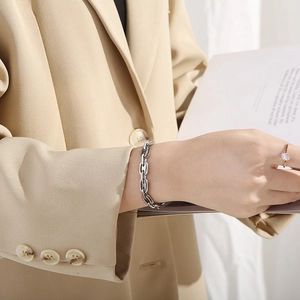 Close-up of a chunky silver coffee bean chain bracelet on a model wearing a beige blazer