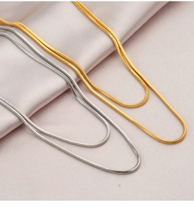 Detail of parallel gold and silver snake chain necklaces on pink satin fabric
