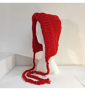 Vue détaillée du bonnet en maille rouge épaisse avec pompons tressés et cache-oreilles