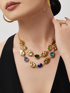 Detail of layered gold necklace featuring green and blue glass stones on a model