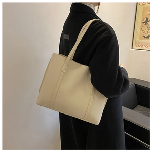 Shoulder view of a large cream white matte leather tote bag in a minimalist setting