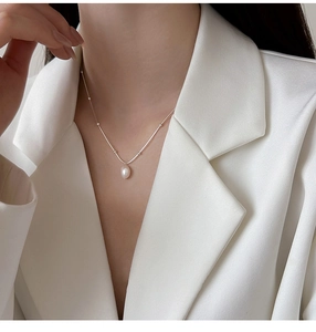 Close-up of a minimalist stainless steel necklace with a baroque pearl pendant on a model