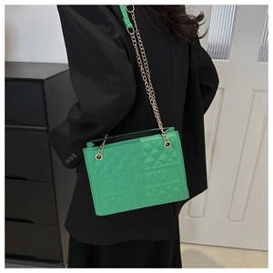 Close-up of green quilted shoulder bag with gold chain strap and embossed fashion text