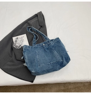 Vue à plat d'un grand sac cabas en denim bleu avec des poches effilochées et accessoires