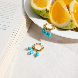 Golden hoop earrings with turquoise beads on a soft fabric background with summer fruit