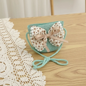 Détail d'un sac en paille vert menthe avec nœud floral et bordure en dentelle blanche