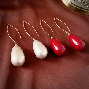 Detail of elegant teardrop pearl earrings in red and white with gold hooks on silk fabric