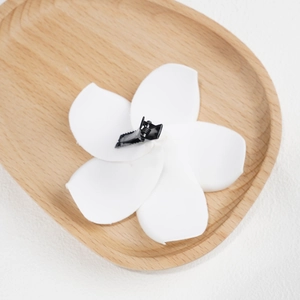 White Plumeria flower hair clip with black metal alligator grip on a wooden tray
