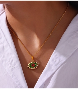 Close-up of evil eye pendant with green enamel and red stone on white shirt model