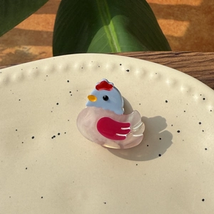 Close-up of a cute cartoon rooster hair clip made of pink and blue acetate on a ceramic plate