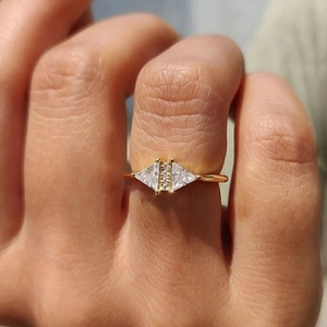 Close-up of a minimalist gold ring with triangle and rectangle zircon stones on finger
