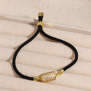 Macro detail of black braided bracelet featuring a gold cylinder charm with pavé cubic zirconia