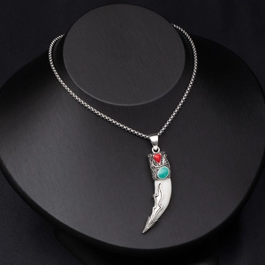 Detailed view of wolf tooth pendant with silver relief, red gemstone, and turquoise inlay
